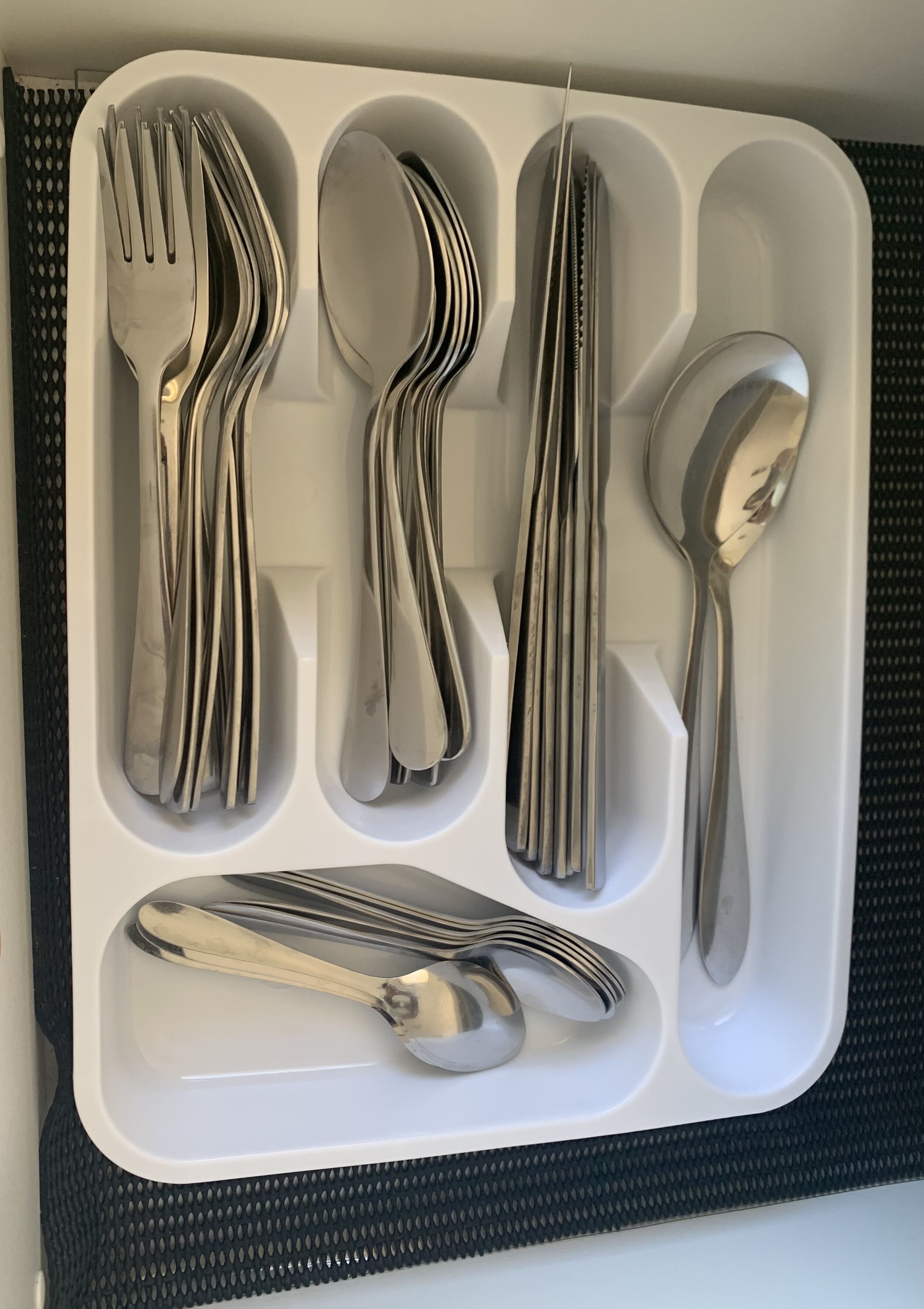 A set of stainless steel utensils neatly arranged in a white compartment.