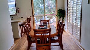 Un coin repas avec une table et des chaises en bois, une vue à travers une porte-fenêtre coulissante et une plante en pot.