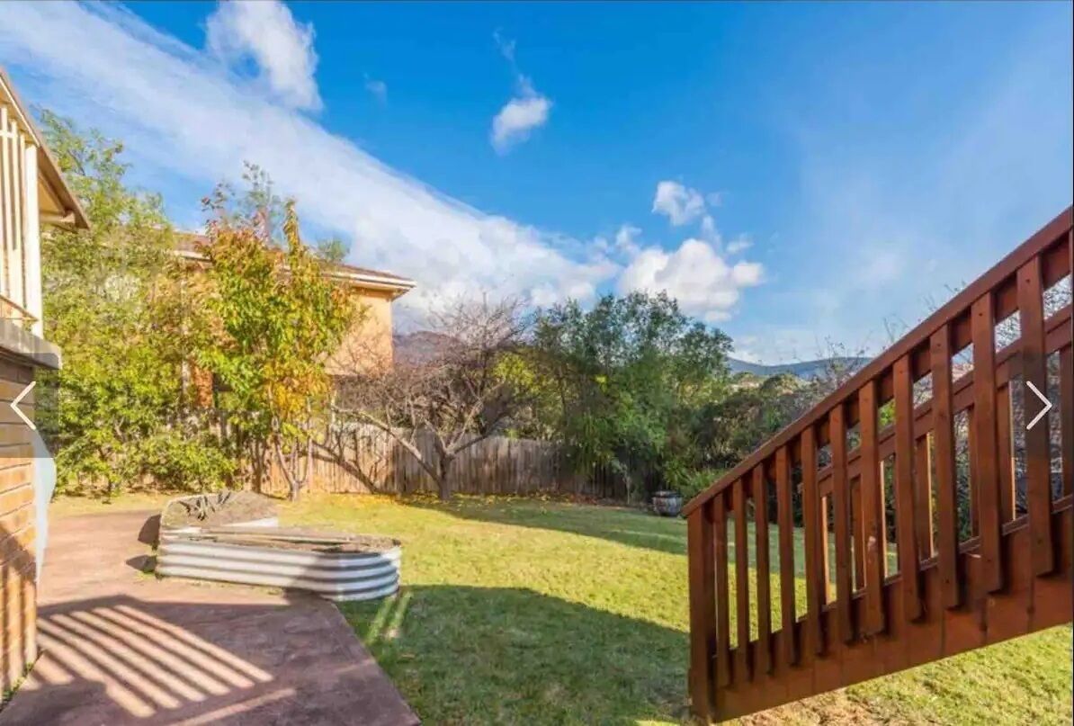 A backyard with a wooden deck, a stone pathway, and a grassy lawn.