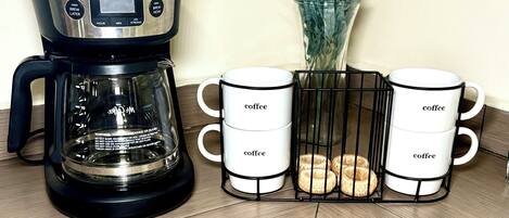 A coffee maker, two coffee mugs, and a vase with lavender flowers.