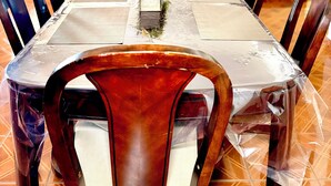 Comedor con una mesa dispuesta para seis personas, sillas, un ventilador de techo y vistas a una sala de estar con sofá y planta.