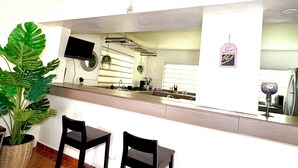 Una cocina moderna con dos taburetes negros, una planta grande en maceta y otra planta colgante.