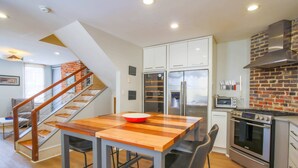A modern kitchen with a wooden table, a refrigerator, an oven, and a brick accent wall. - Walk to Upper King!  Renovated Kitchen, Double Piazzas.  Original Charleston Home Experience. (Charleston)