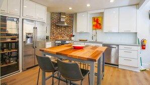 A modern kitchen with white cabinets, a stainless steel refrigerator, a wooden table, and two chairs. - Walk to Upper King!  Renovated Kitchen, Double Piazzas.  Original Charleston Home Experience. (Charleston)