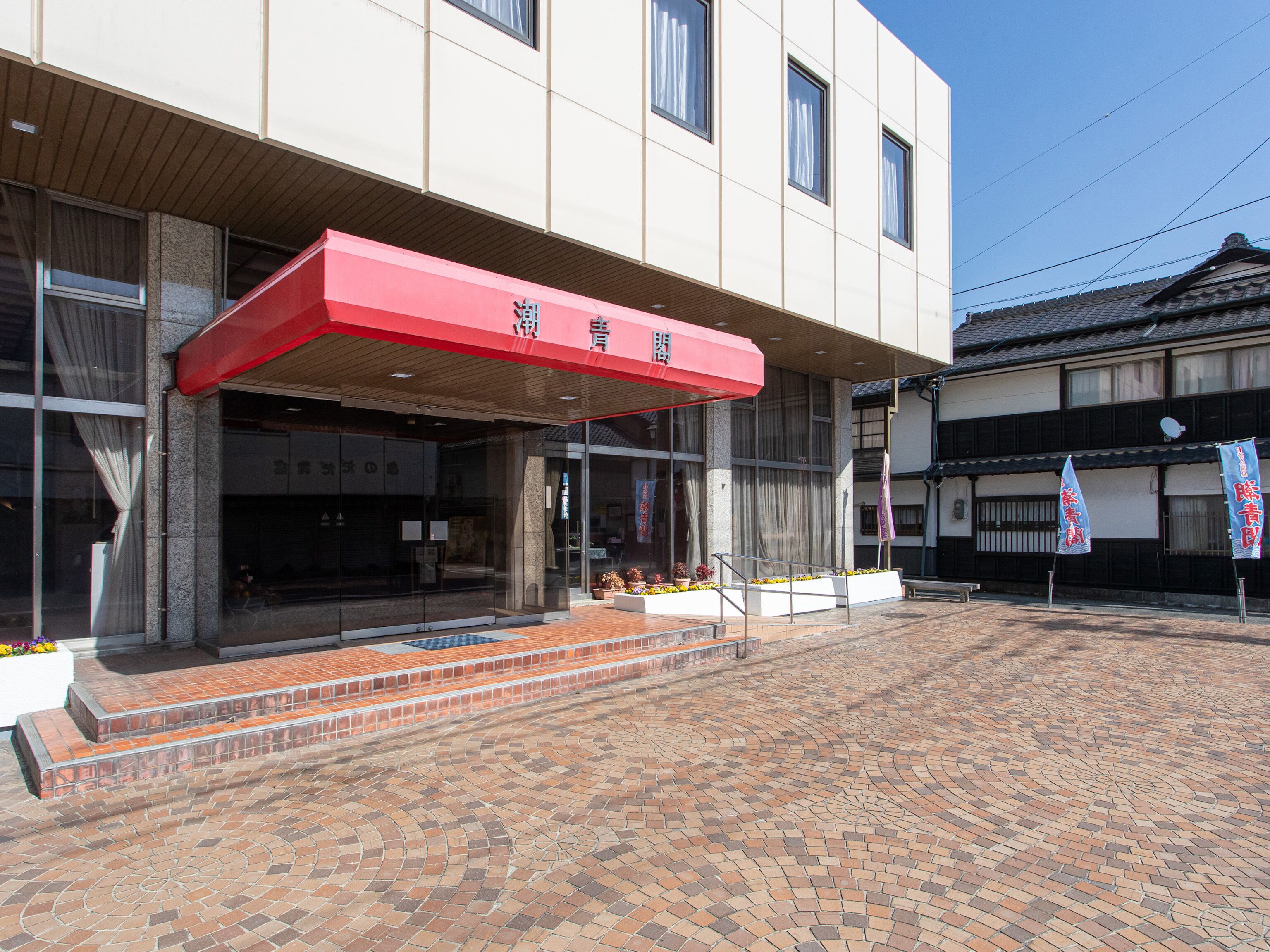 A building with a red awning, a tiled courtyard, and traditional Japanese architecture.