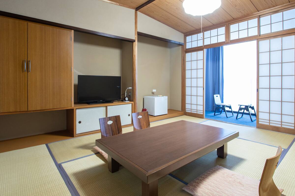 Een traditionele Japanse kamer met tatami vloeren, een lage houten tafel, een televisie en schuifdeuren.