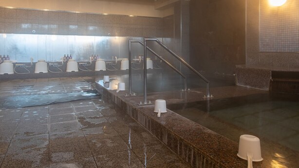 A steam room with a wet floor, a glass partition, and a seating area with a white chair. - Tabist Hotel Chouseikaku (Yatsushiro)