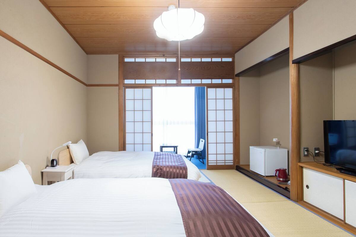 Een hotelkamer met twee bedden, een televisie, een tafeltje en uitzicht buiten via een schuifdeur.
