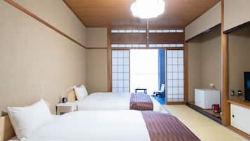 A traditional Japanese-style hotel room with two beds, a small table, a chair, a television, and a refrigerator.
