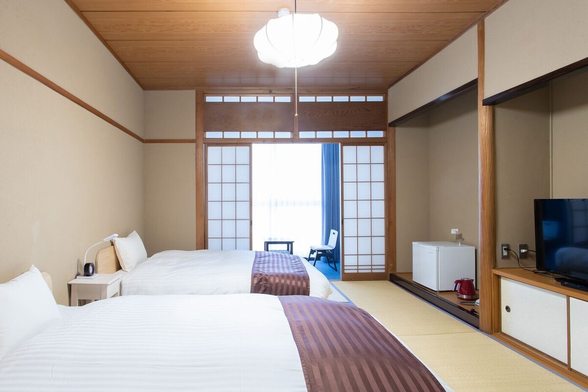 Habitación de hotel con dos camas, televisión, escritorio y vistas al exterior.