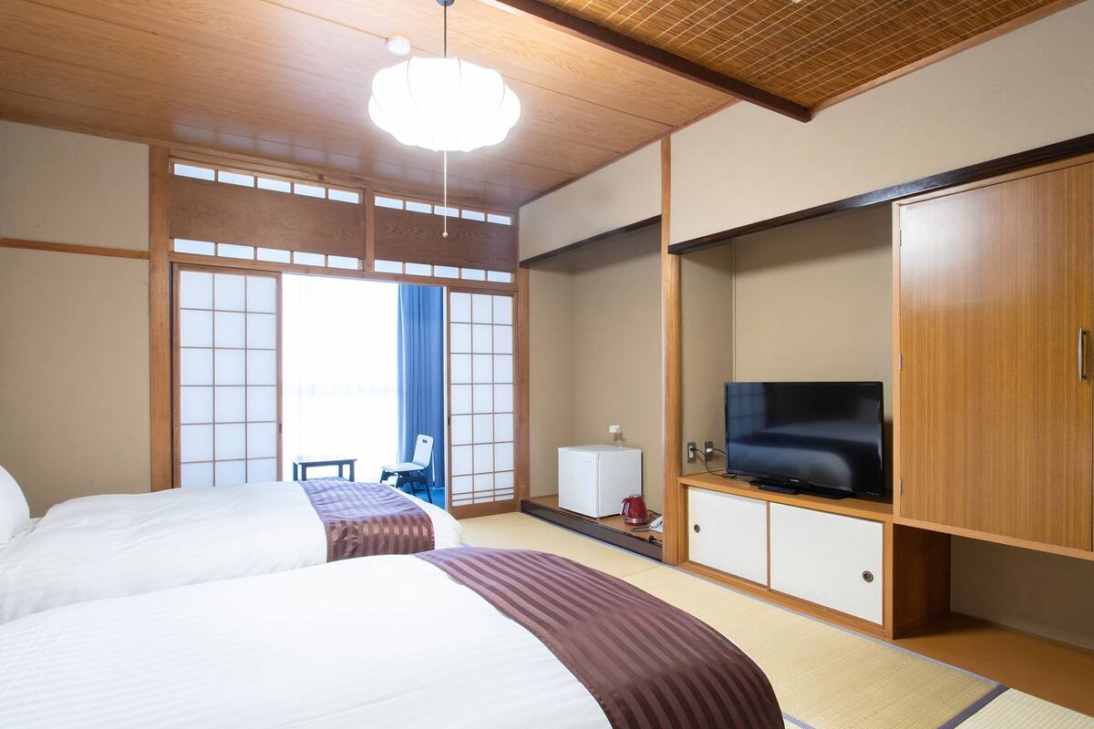 Een hotelkamer met twee bedden, een televisie, een klein tafeltje met waterkoker, en schuifdeuren.