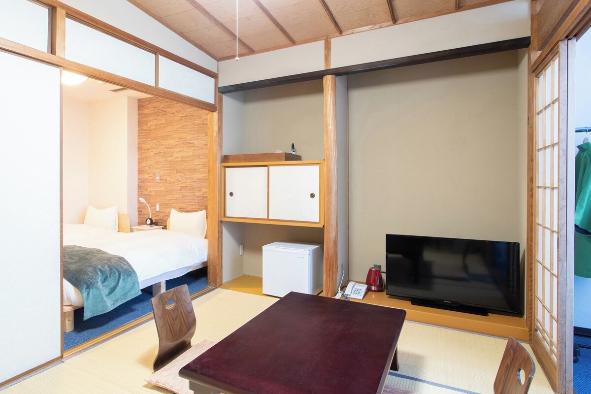 Una habitación de hotel con una cama, televisión, escritorio pequeño y armario.