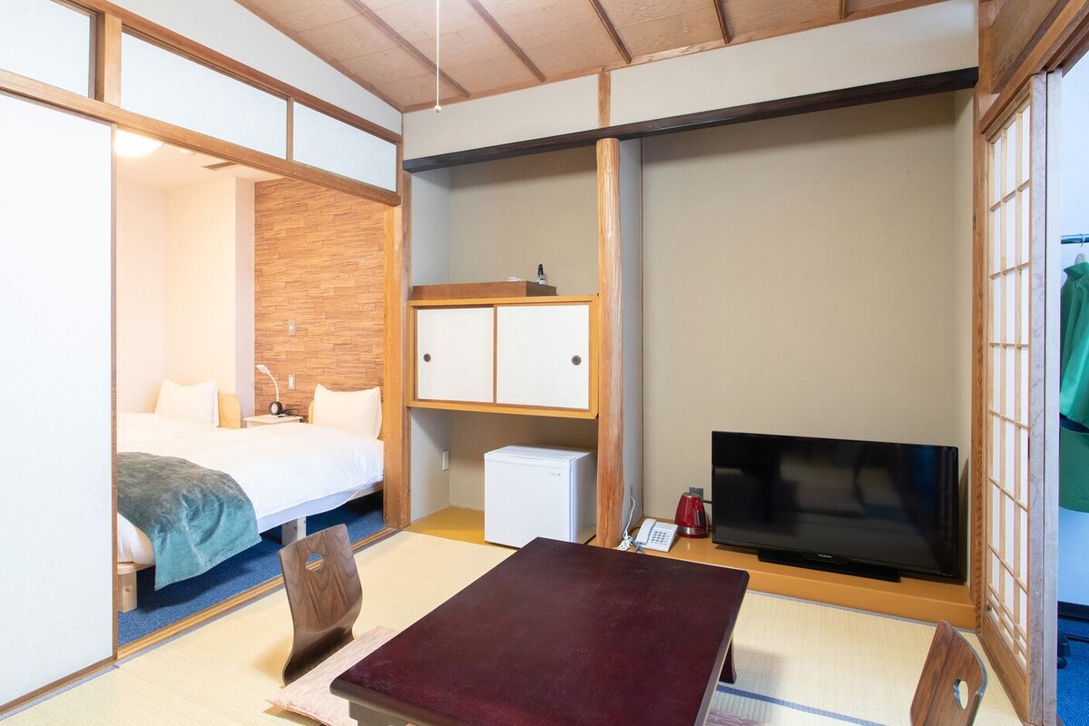 Una habitación con cama, escritorio, televisor y refrigerador pequeño.