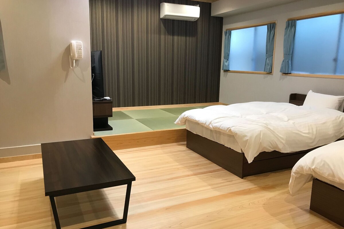 Una habitación de hotel moderna con cama, mesitas de noche, un escritorio pequeño, teléfono en la pared y un equipo de aire acondicionado.