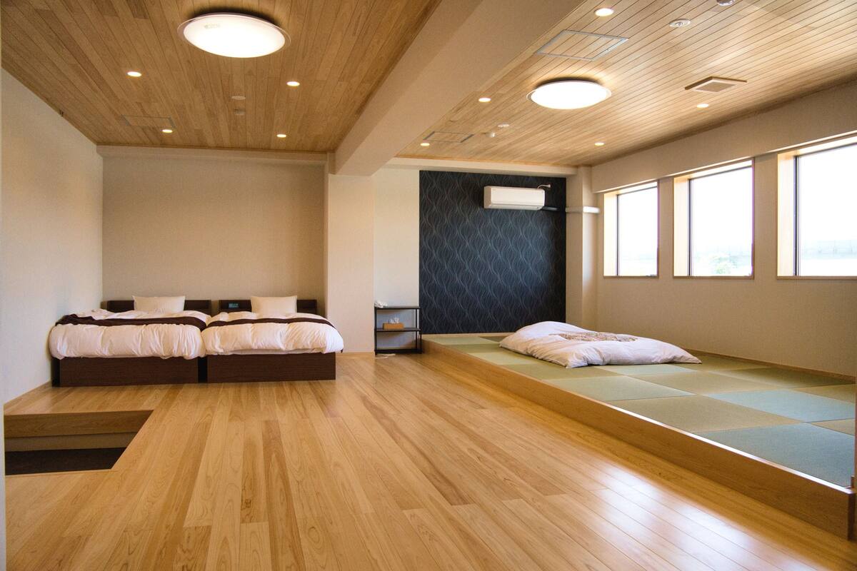 Een moderne hotelkamer met twee bedden, een ingebouwde bank, houten vloeren en grote ramen.