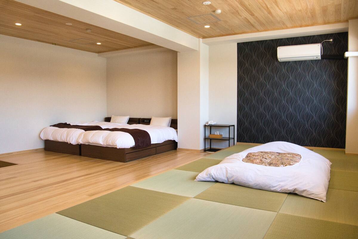 Een moderne slaapkamer met een houten plafond, een bed met witte beddengoed en een futon met een kussen.