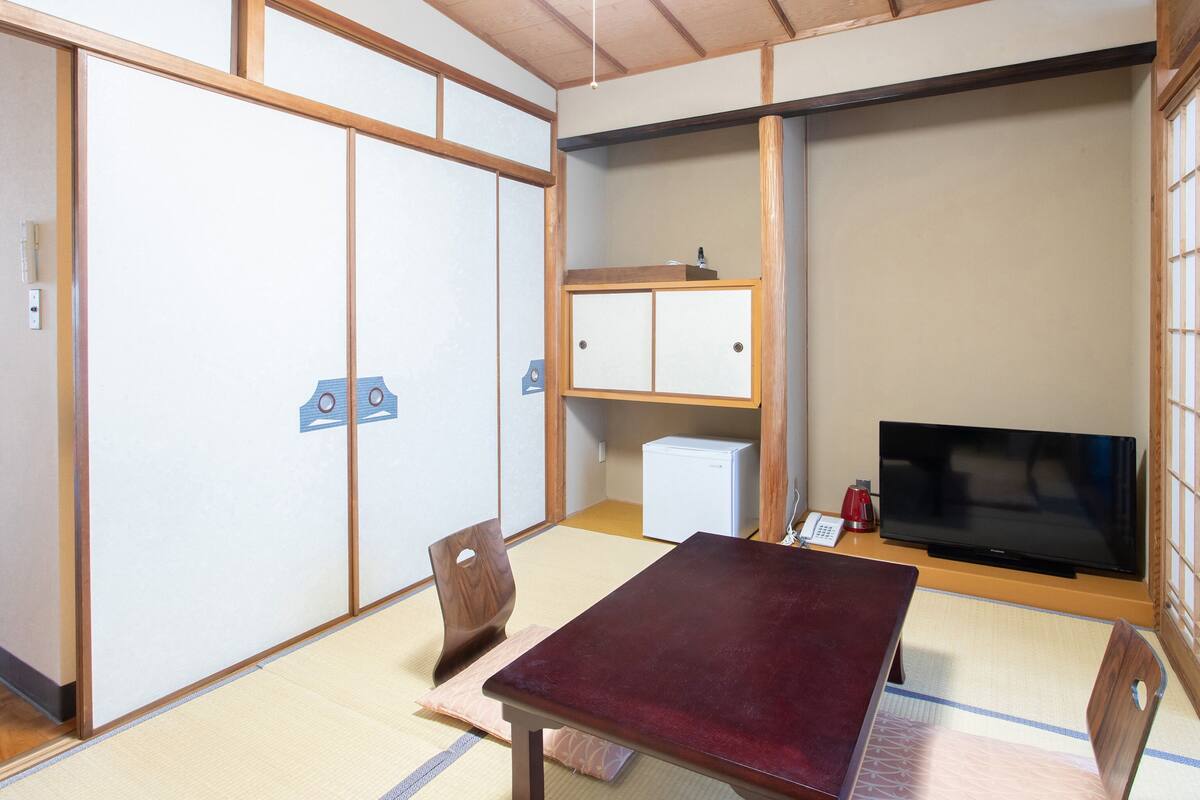 Een traditionele Japanse kamer met tatami vloeren, een lage tafel, een televisie en een kast.