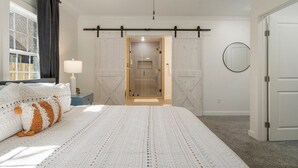 Ein Schlafzimmer mit einem großen Bett, einem Deckenventilator, einer Schiebetür im Bauernhausstil und Blick ins Badezimmer.