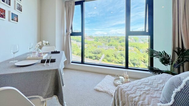 Habitación de hotel con un ventanal grande, una mesa de comedor dispuesta con platos, vasos y un jarrón de flores.