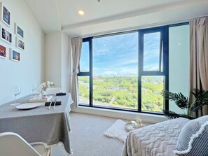 A hotel room with a large window, a dining table set with plates, glasses, and a vase of flowers. - Chic Studio with Pool in CBD (Auckland)