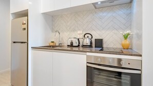 Una cocina moderna con armarios blancos, encimera de granito, horno empotrado, hervidor, tostadora y una pequeña planta en maceta.