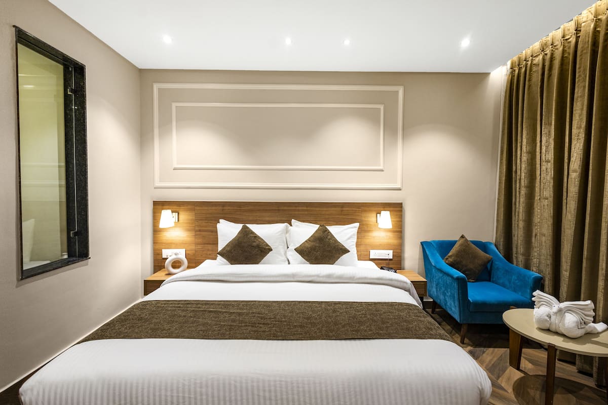 Habitación de hotel con una cama grande, dos mesitas de noche con lámparas, un sillón azul y una pequeña mesa con toallas.