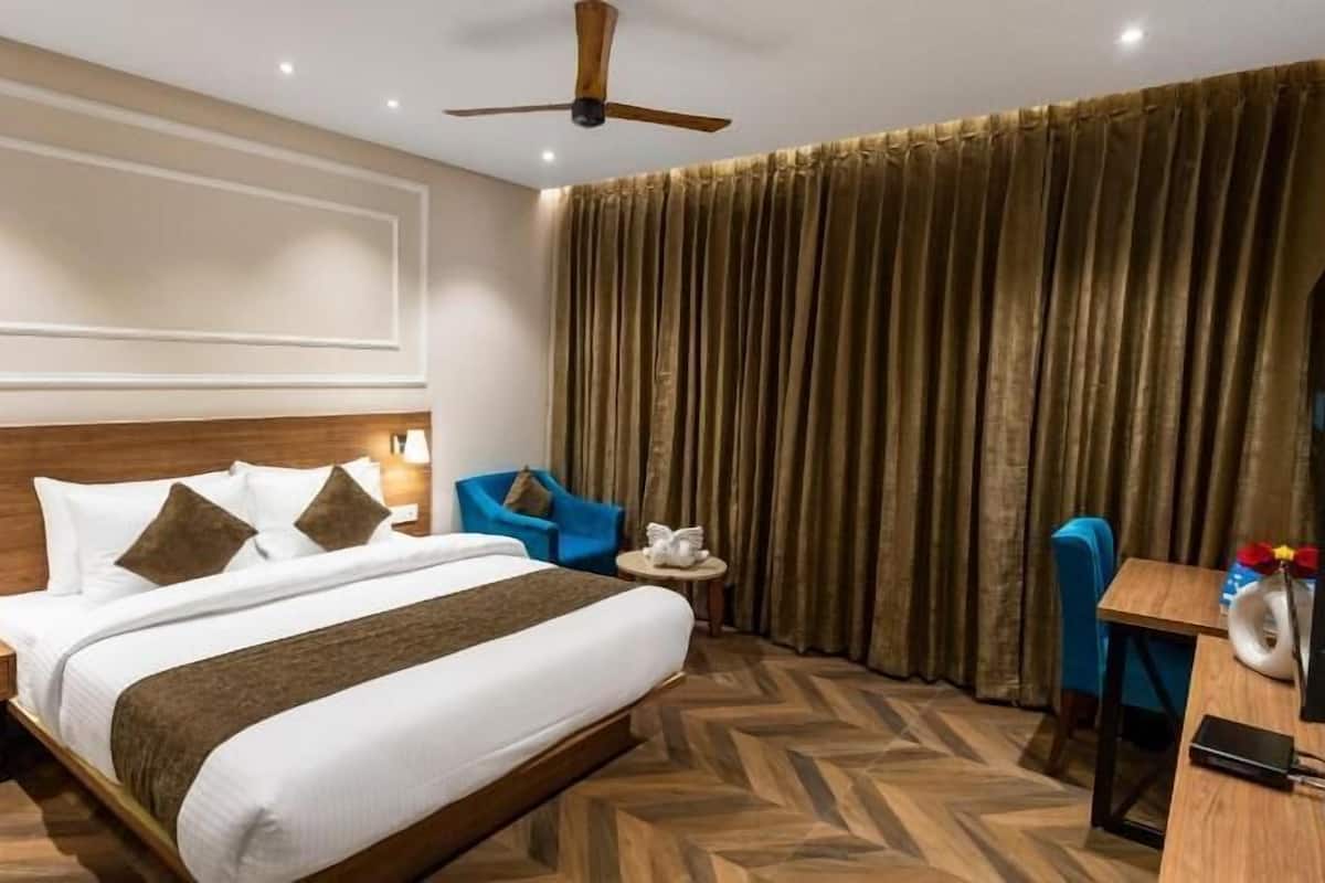 Habitación de hotel con una cama grande, un escritorio, una silla, un ventilador de techo y cortinas.
