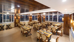 Un ristorante con diversi tavoli e sedie, ampie finestre e un soffitto in legno.