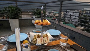 Tavola imbandita per un pasto, con piatti, posate e una tazza di tè, affacciata su un panorama urbano e montuoso.