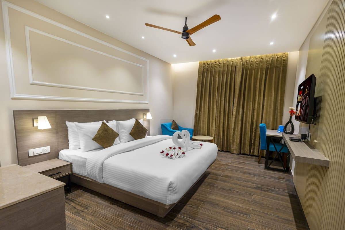 Habitación de hotel con cama, mesita de noche, lámpara, ventilador de techo, cortinas y escritorio con silla.