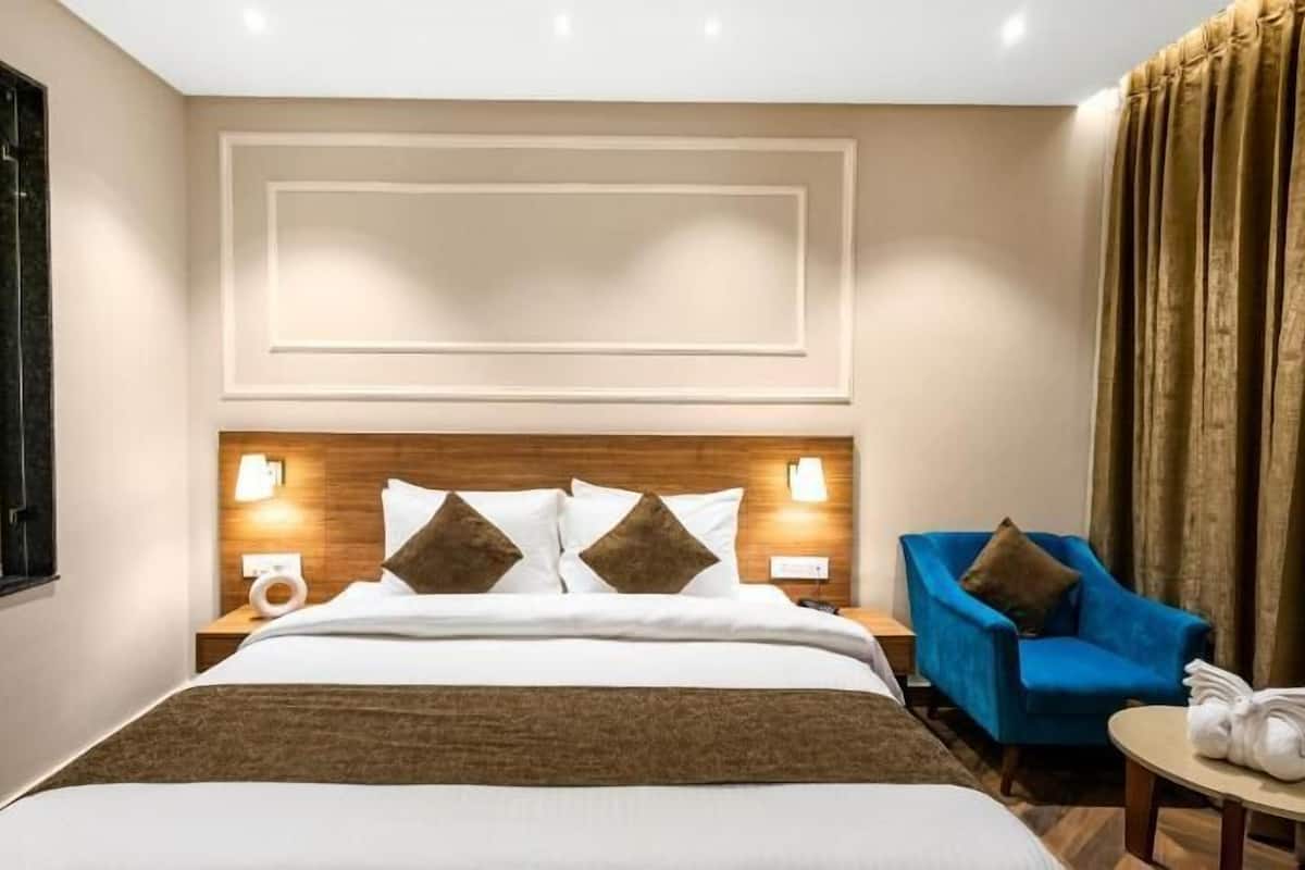 Una habitación de hotel con una cama, un sillón azul, una mesita y un ventanal.