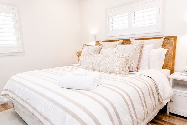 A neatly made bed with striped bedding, a bedside table with a lamp, and a window with blinds.