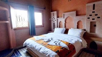 Una habitación con cama, ventana con cortinas, equipo de aire acondicionado y alfombras estampadas.
