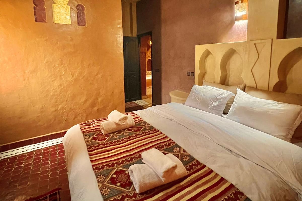 A hotel room with a large bed, a patterned rug, and a small table with towels.