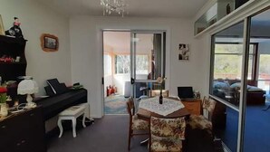 Olohuoneessa on piano, ruokapöytä tuoleineen, sohva ja suuri ikkuna.