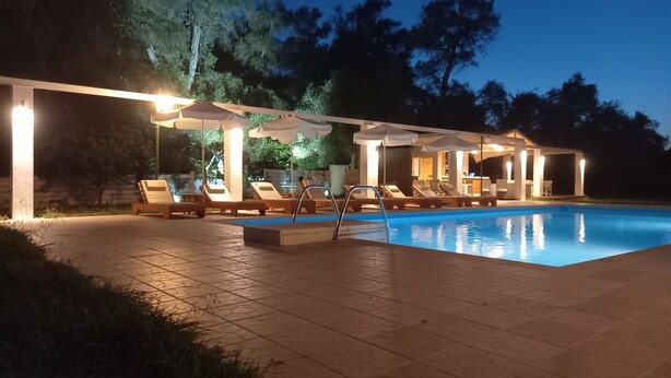 A poolside area with lounge chairs and umbrellas, a pool, and a covered seating area. - Amelia's Garden (Corfu)