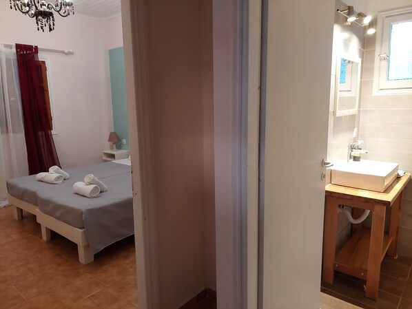 Habitación de hotel con cama, mesita de noche con lámpara, baño con lavamanos y espejo, y un candelabro.