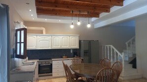 A modern kitchen with white cabinets, a built-in oven, and a dining table with chairs. - Amelia's Garden (Corfu)