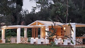 A covered outdoor seating area with white furniture and a bar area. - Amelia's Garden (Corfu)