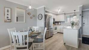 Eine moderne Küche mit weißen Schränken, Edelstahlgeräten und einem Essbereich mit rundem Tisch und weißen Stühlen.