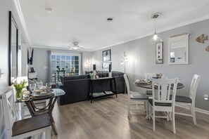 A modern living room with a dining area, grey walls, wooden flooring, and a ceiling fan.