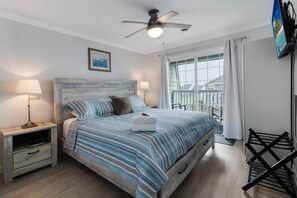 A bedroom with a bed, nightstands, a ceiling fan, a TV, and a window with curtains.