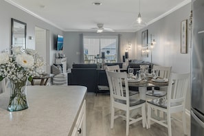 A modern kitchen with a dining area, white furniture, and a large window.