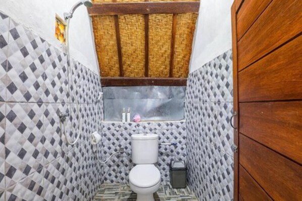 Un baño con piso de baldosas a cuadros, un inodoro blanco, un ventanal pequeño con persiana tejida y un armario de madera.
