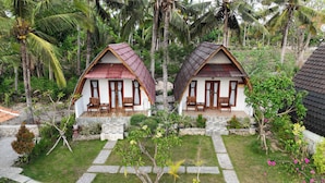 Two small, identical cottages with red roofs and white walls, surrounded by lush greenery and palm trees. - Diamond Beach Bungalow (Penida Island)