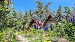 A tropical resort with two wooden-roofed cottages surrounded by lush greenery and palm trees. - Diamond Beach Bungalow (Penida Island)