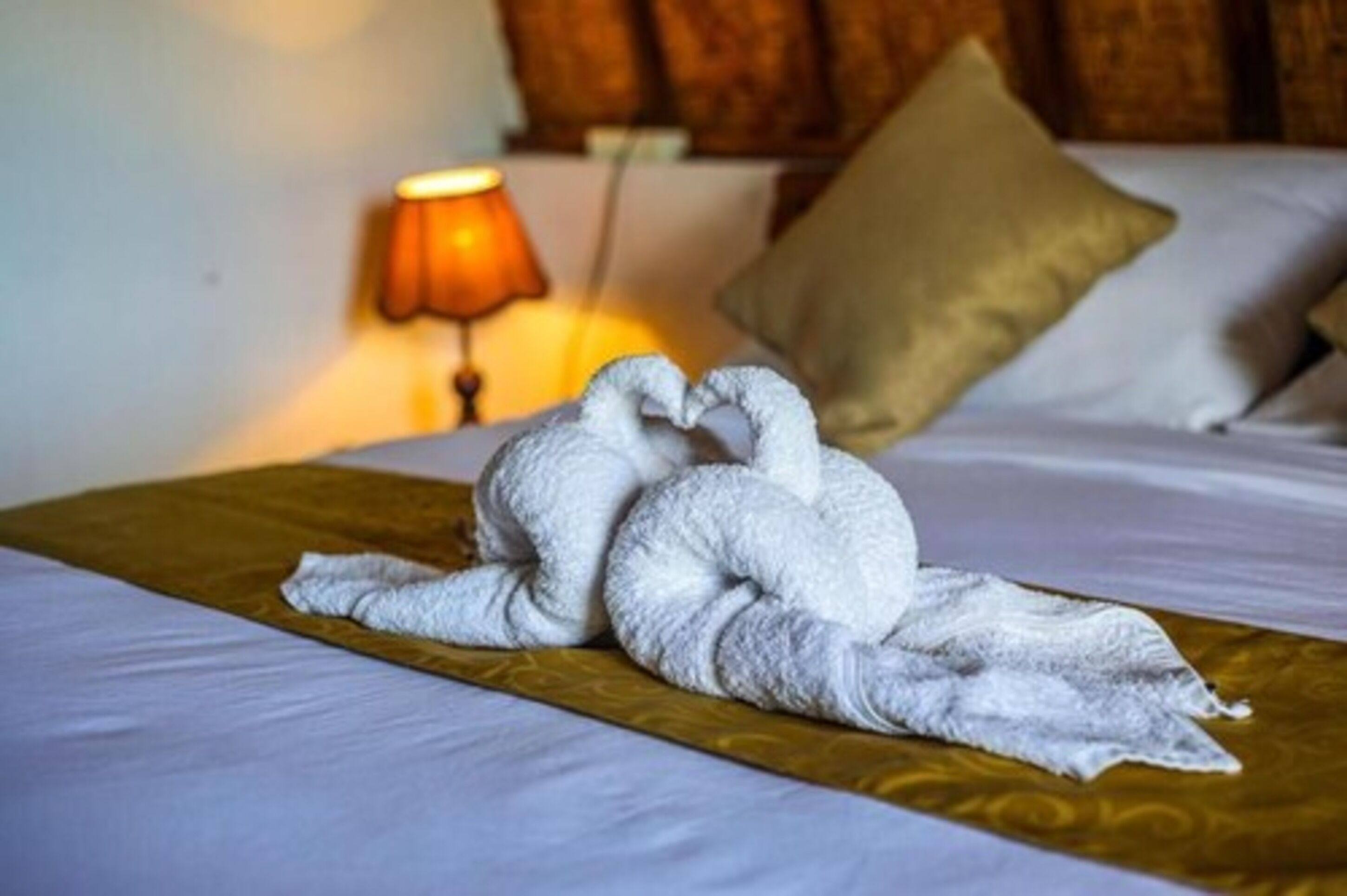 A bed with a golden bedspread and a towel arranged in the shape of two swans.