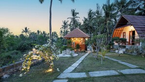 A small, cozy house with a tiled roof, surrounded by lush greenery and palm trees. - Diamond Beach Bungalow (Penida Island)