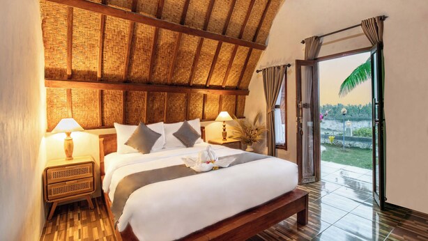 A room with a bed, nightstands, a lamp, a window with curtains, and a view of the outdoors. - Diamond Beach Bungalow (Penida Island)