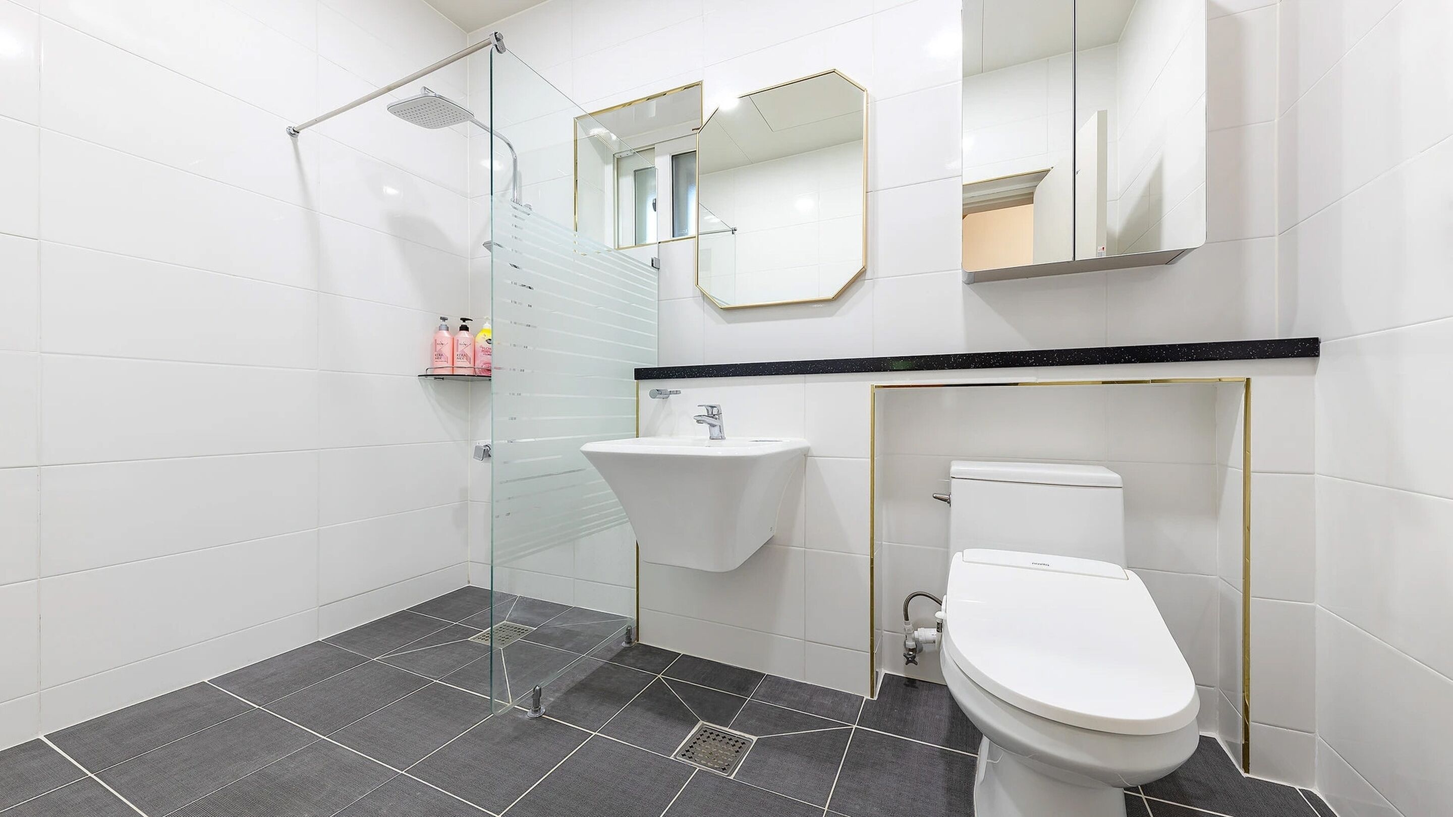 Un baño moderno con cabina de ducha de vidrio, un lavamanos blanco y un inodoro.